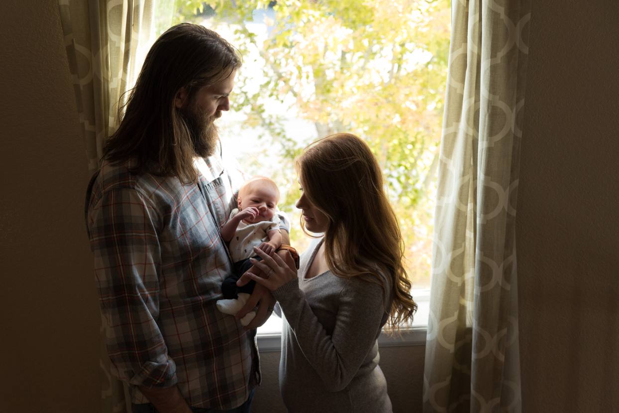 Mom and dad holding baby while standing in front of window