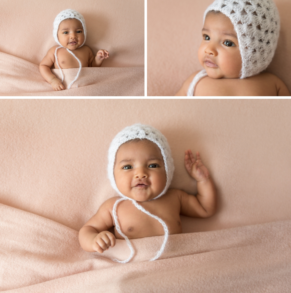 Awake newborn poses under blankets with white bonnet