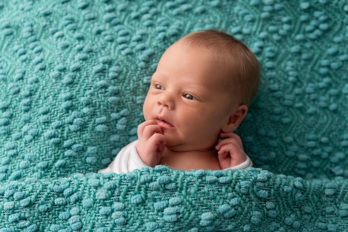 Pensive newborn on turquoise backdrop