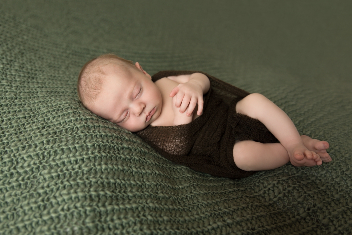 Newborn baby boy on a sage green drop with dark brown wrap