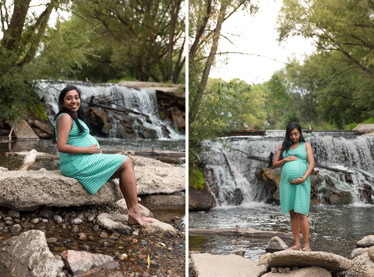 Pregnant woman with black hair and a turquoise maternity dress standing next to a waterfall