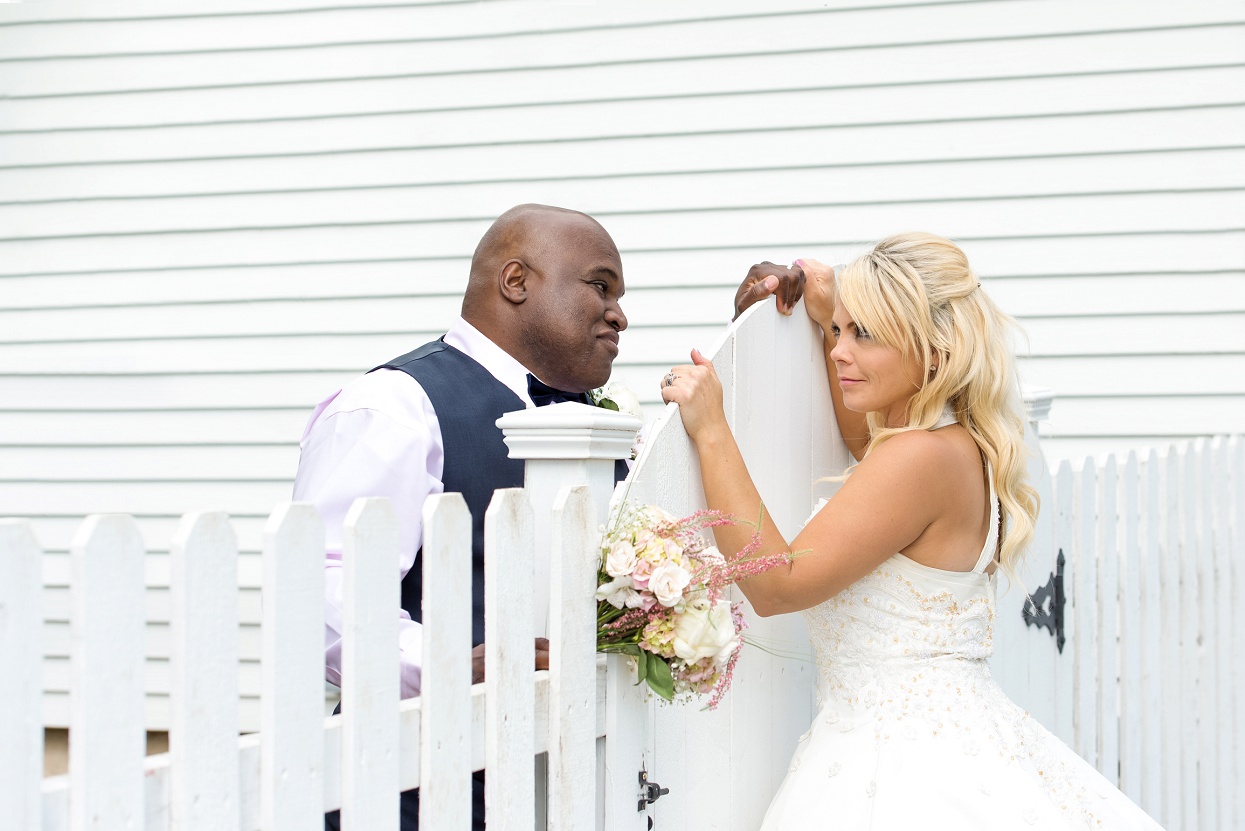 Bride and groom posing with a white picket fence, playful couple posing