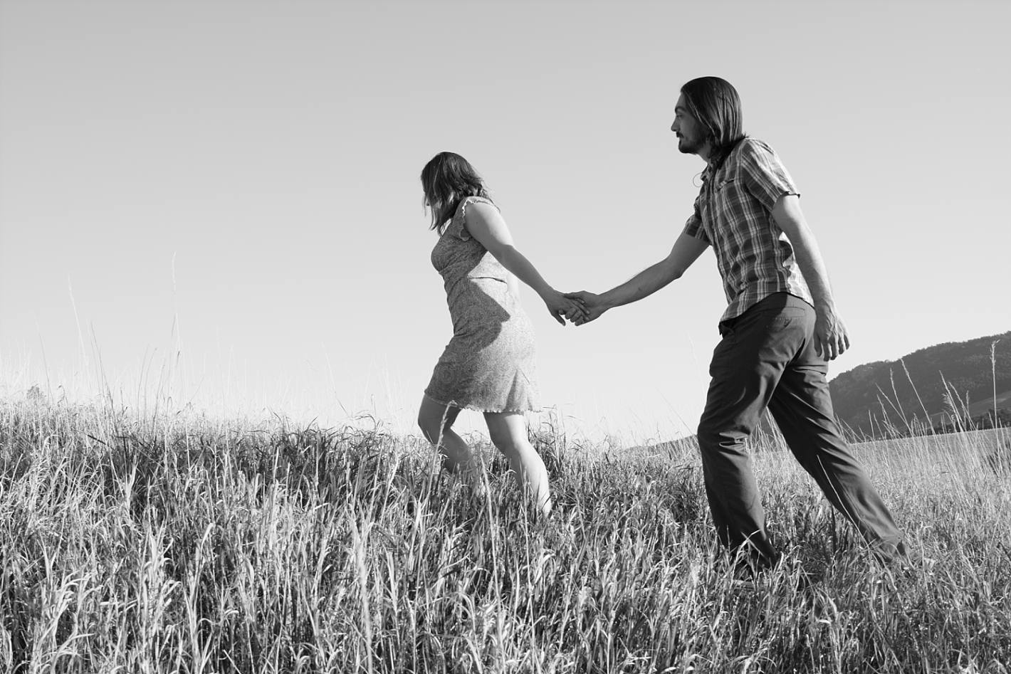 Woman leading man through grass, black and white engagement photography