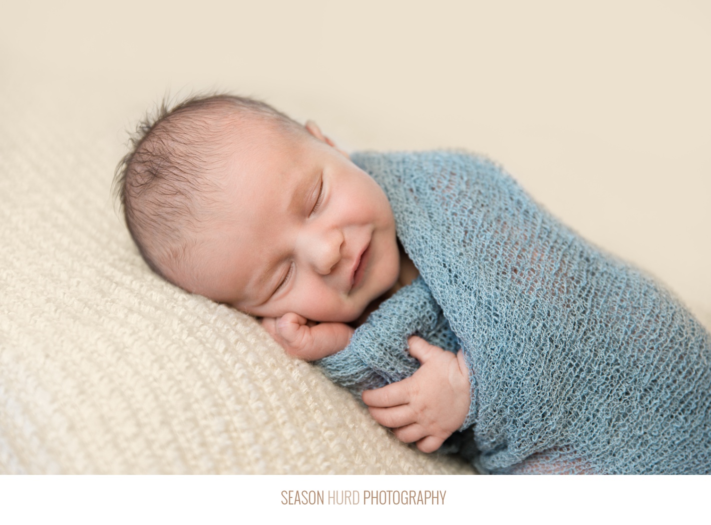 Newborn photography with baby wrapped in ice blue on a tan background