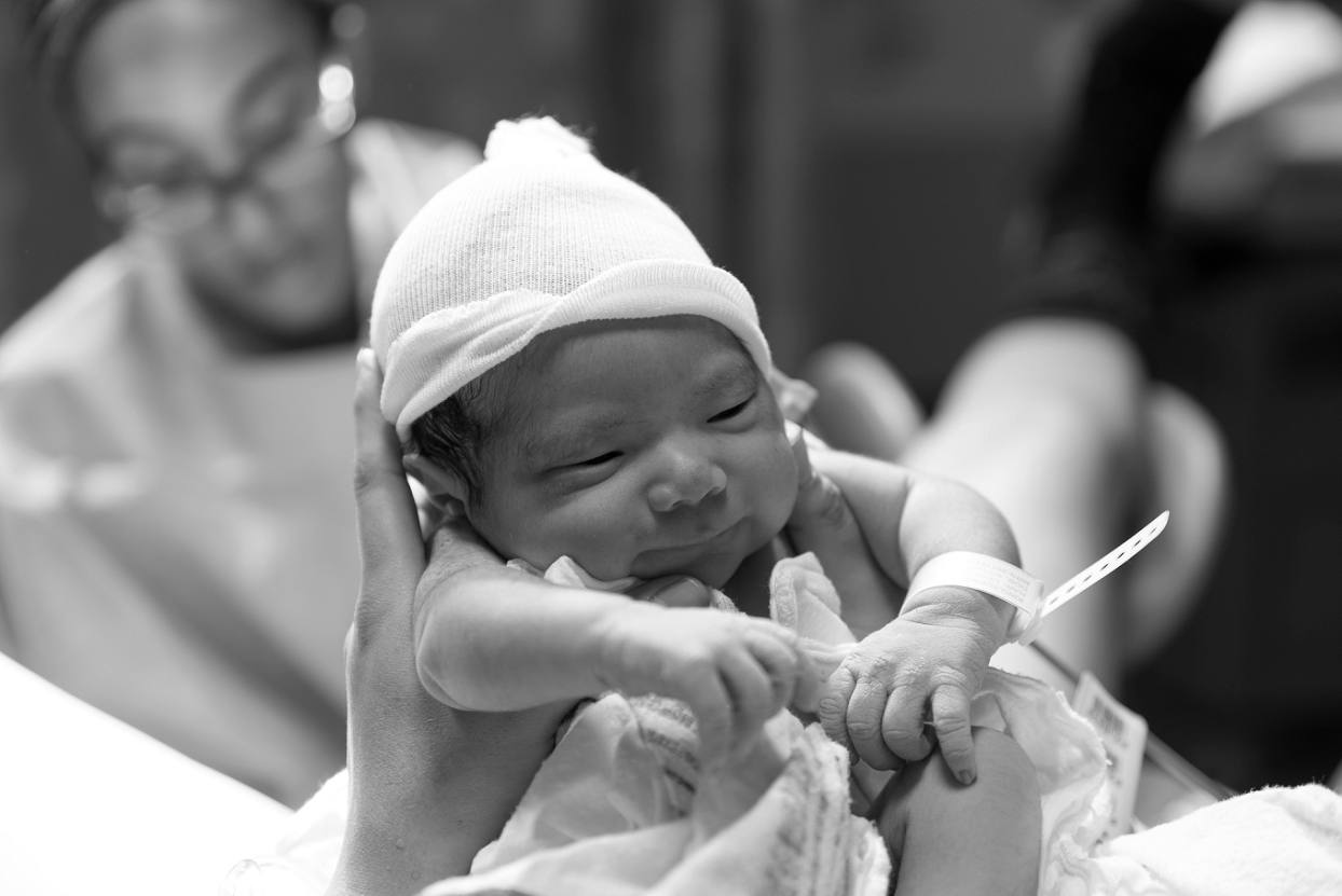 Newborn smiles while doctor work behind him